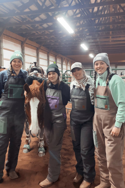 Four people in overalls standing with a horse inside a barn.
