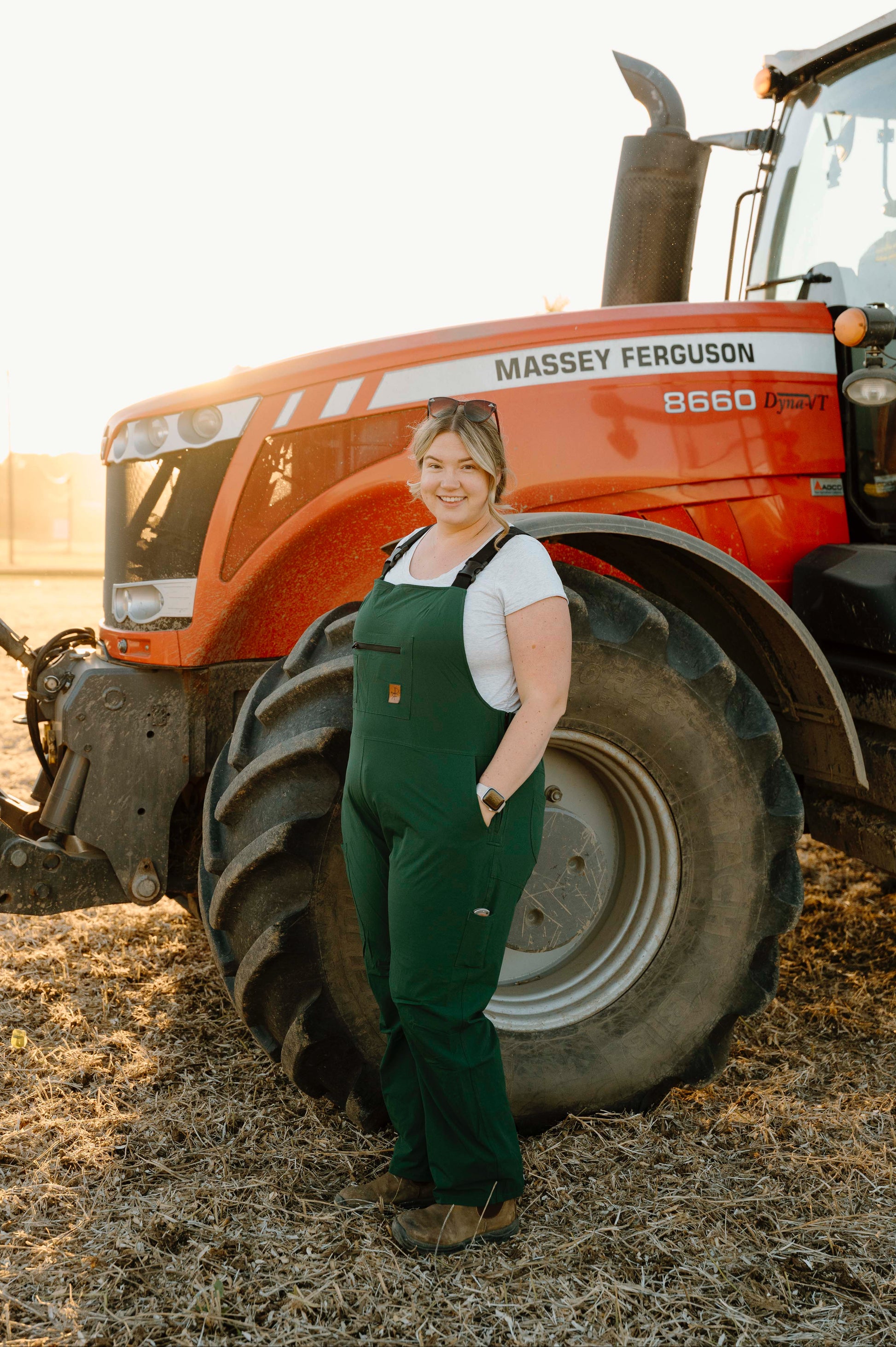Person in green overalls standing next to a Massey Ferguson tractor on a farm.