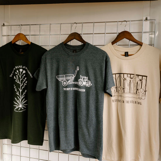 Three t-shirts with different designs hanging on a rack against a white tiled wall.