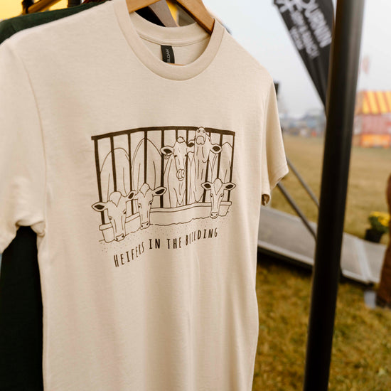 Beige t-shirt with graphic design on a hanger against an outdoor event backdrop