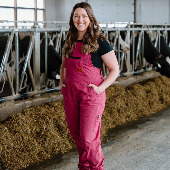 Woman in pink overalls standing in a barn with cows.