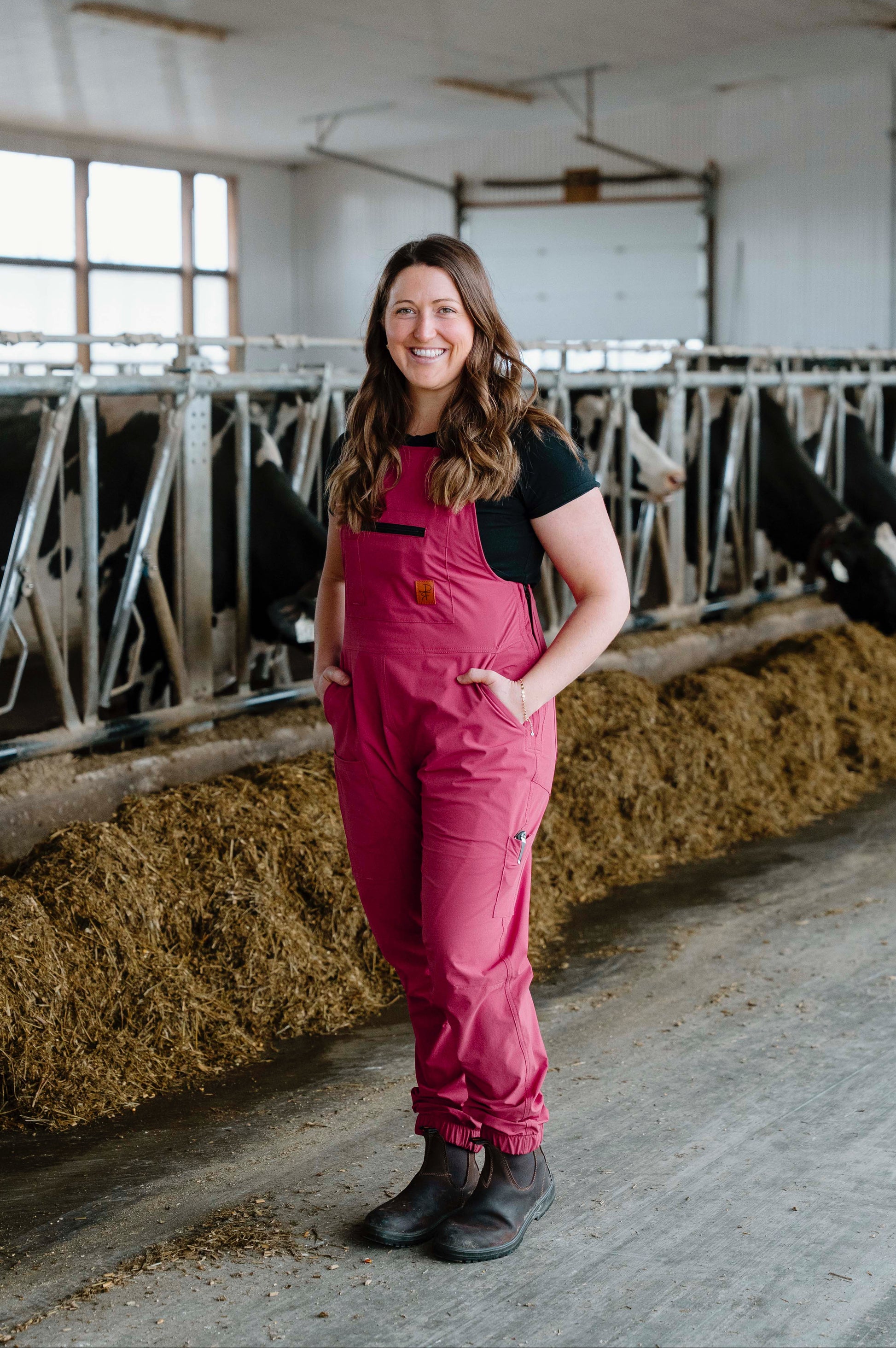 Woman in pink overalls standing in a barn with cows.