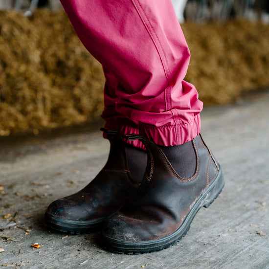 Person wearing pink overalls and black boots on a wooden floor with hay in the background