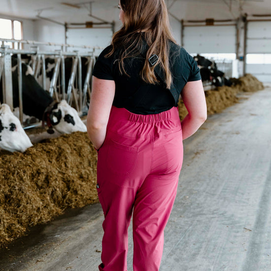 Person walking in a barn with cows and hay bales.