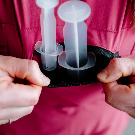 Person holding a black case with two clear plastic items inside, against a pink background.