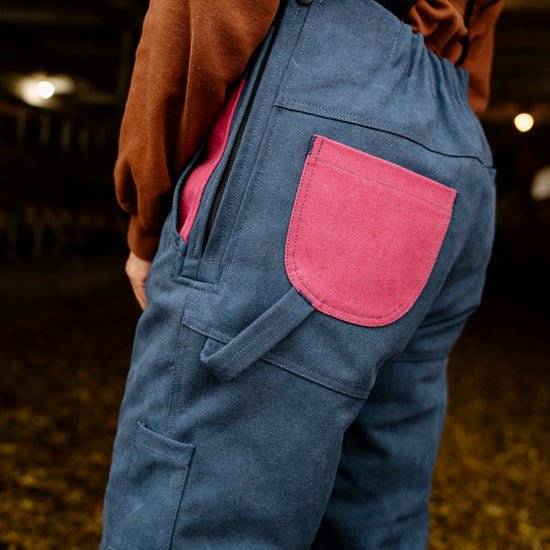 Blue overalls with a pink pocket worn by a person, blurred background