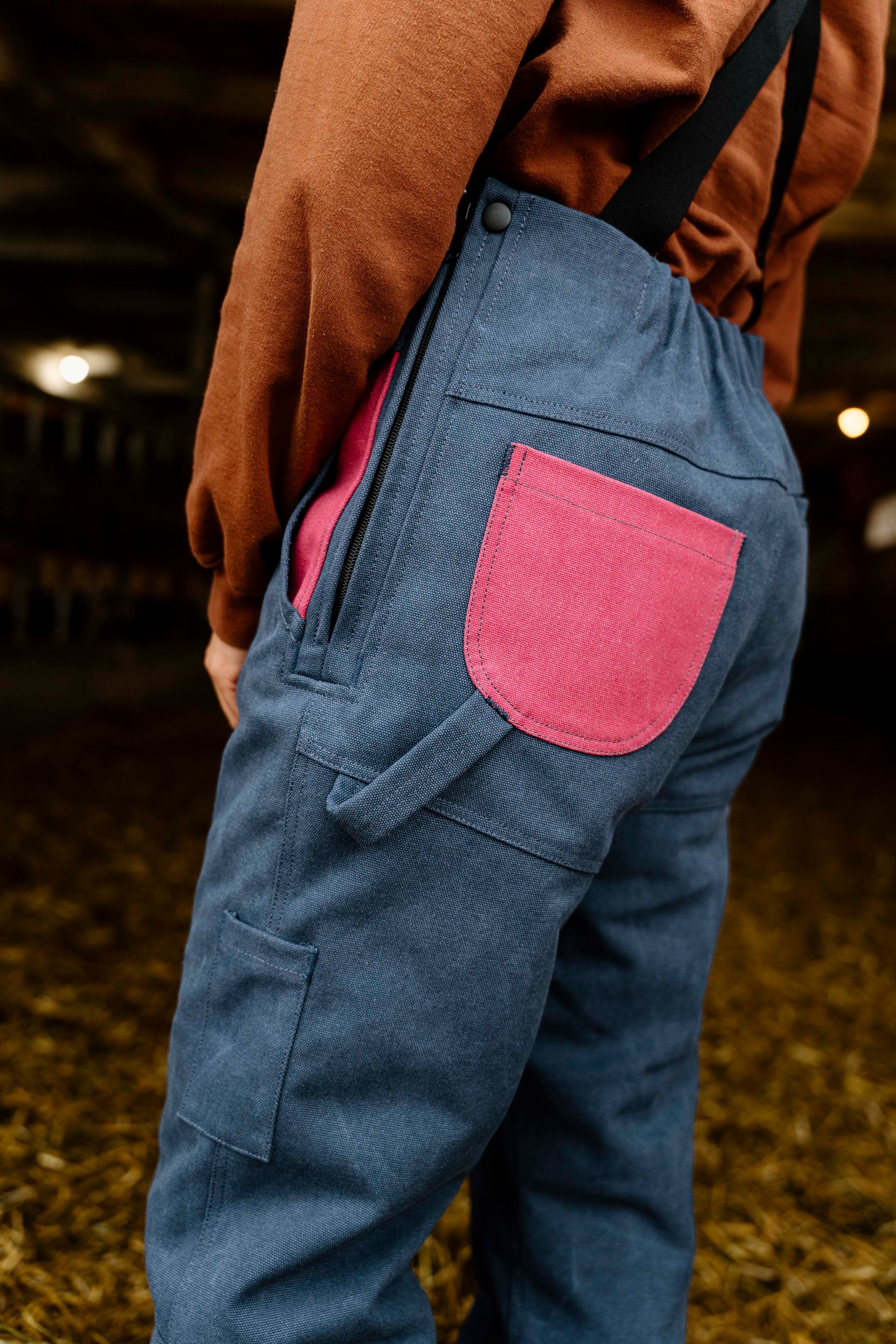 Blue overalls with a pink pocket worn by a person, blurred background