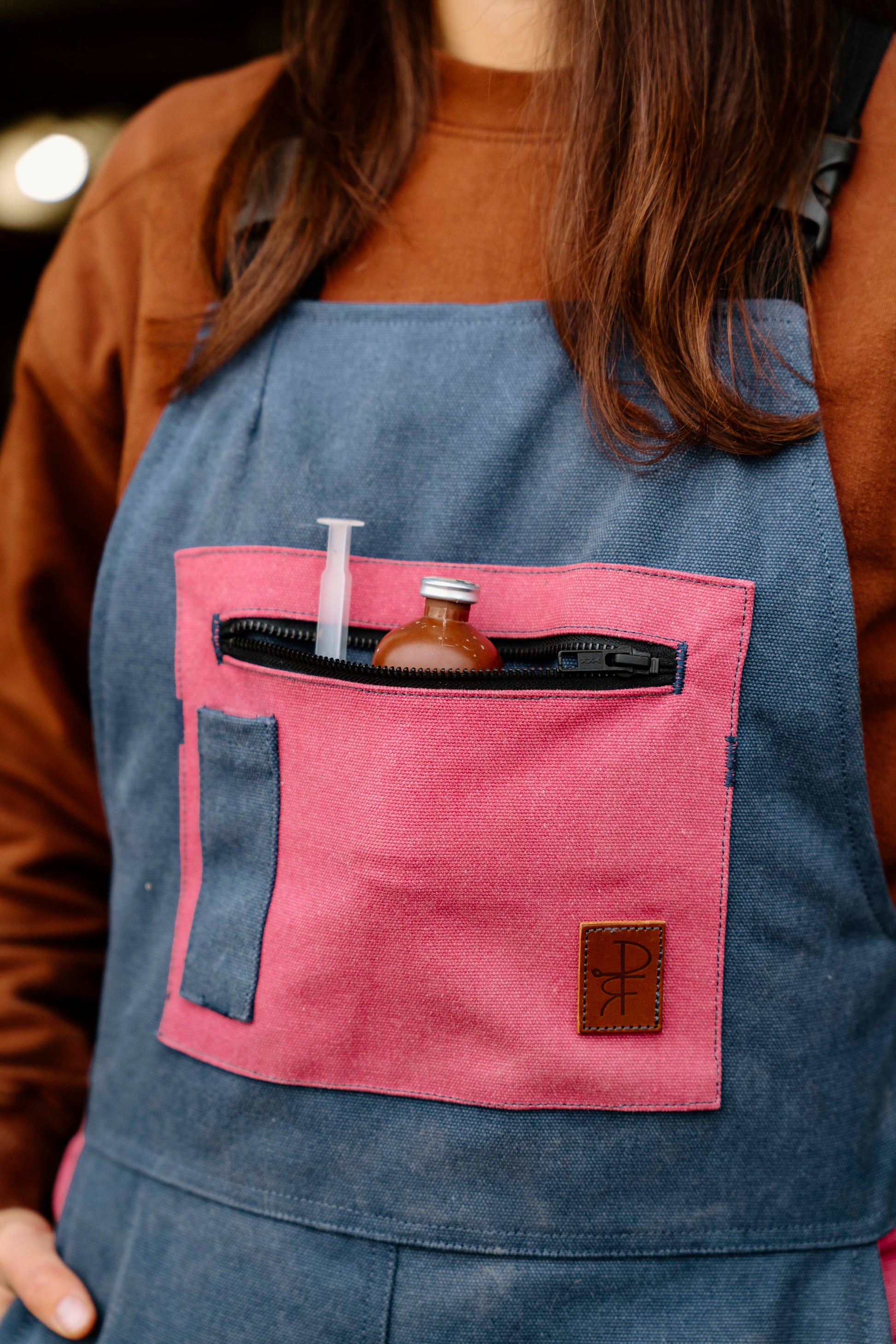 Person wearing a blue overalls with pink pocket containing tools.