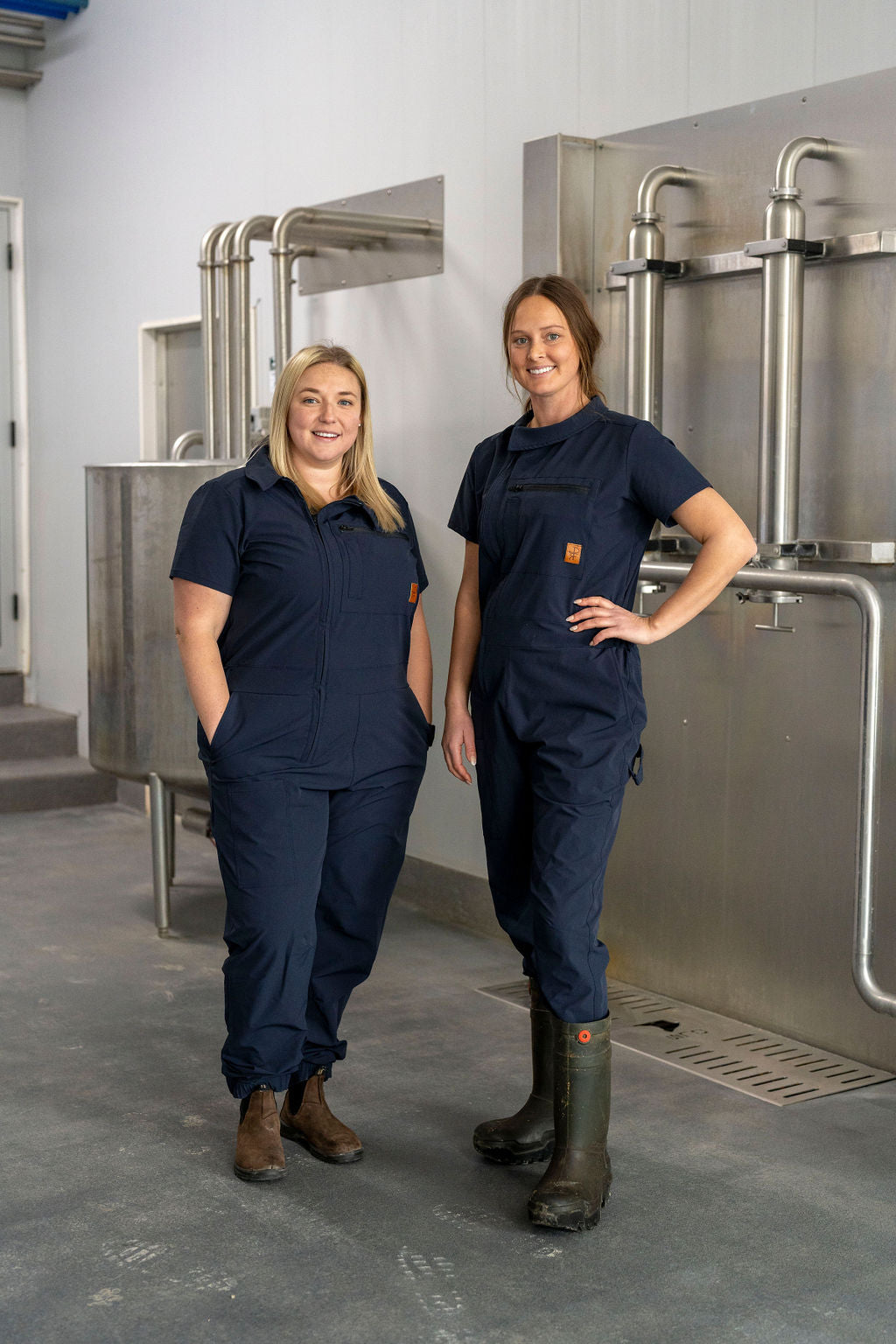 Two individuals wearing navy blue short-sleeved quick dry coveralls, standing in front of industrial equipment.