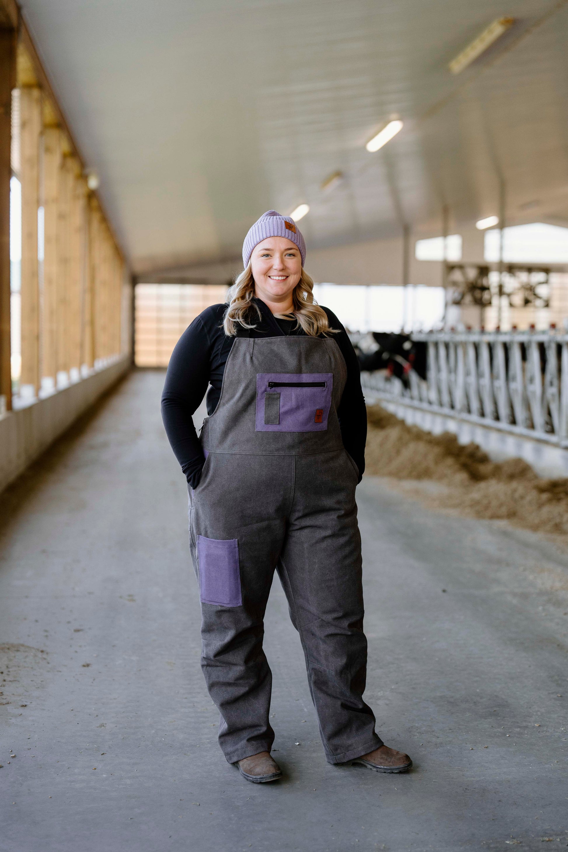 A person wearing a purple and gray insulated overall, standing in a barn setting.