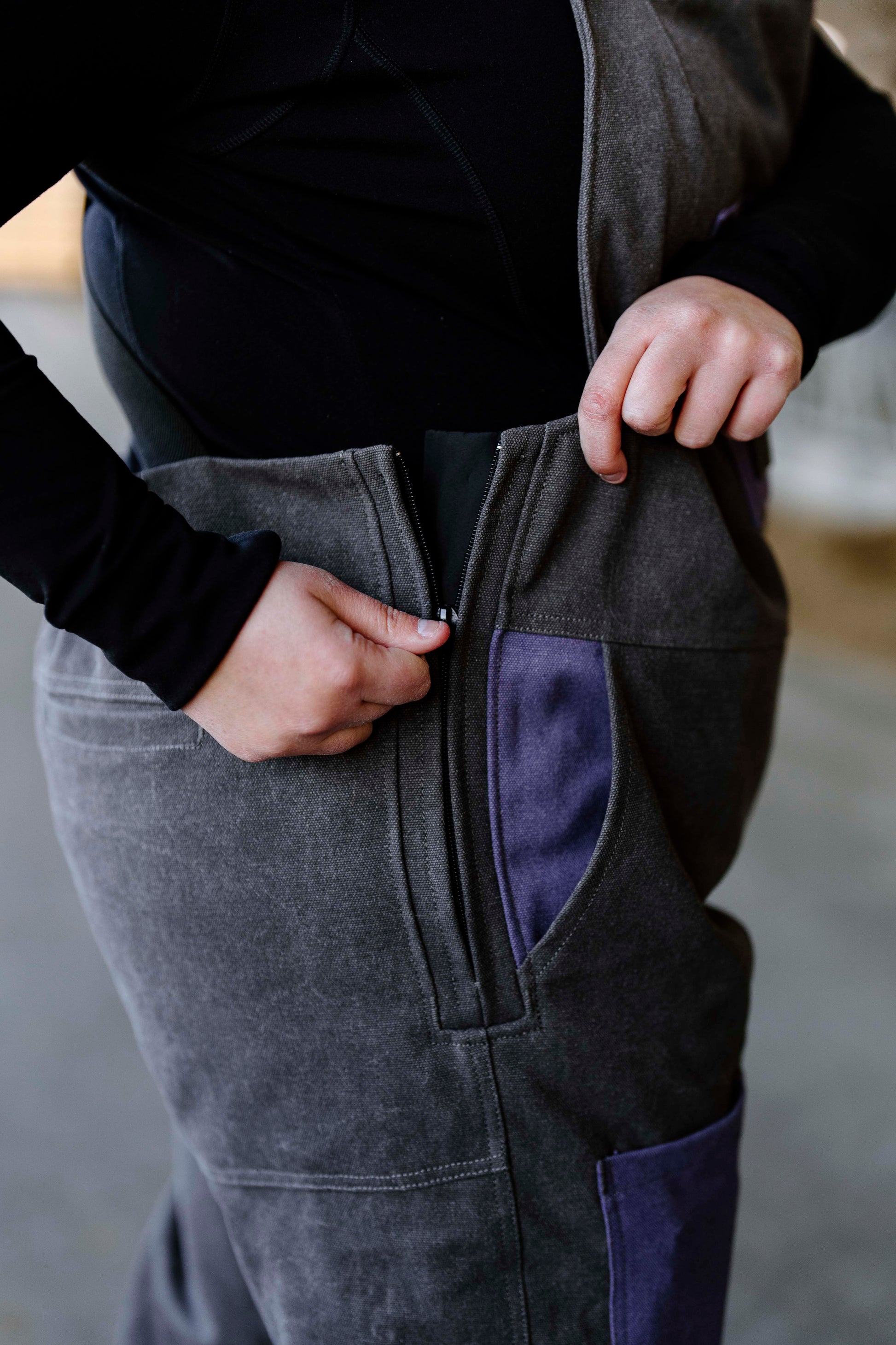 Person un-zipping grey overalls with purple pockets 